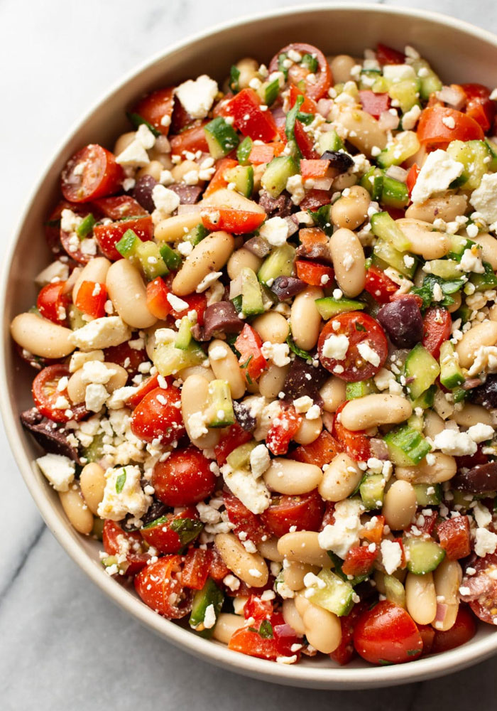 A Lunch idea featuring a vibrant Mediterranean bean salad with white beans, cherry tomatoes, cucumbers, olives, feta cheese, and chopped bell peppers.