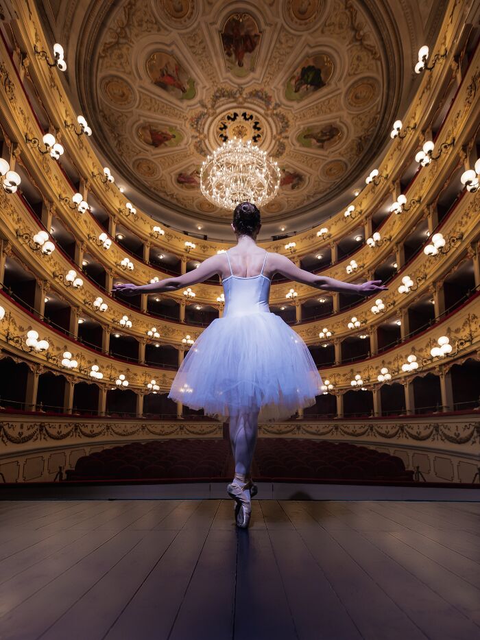 Ballerina on stage in an ornate theater, showcasing elegance and grace, captured in a 2023 Budapest International Foto Award.