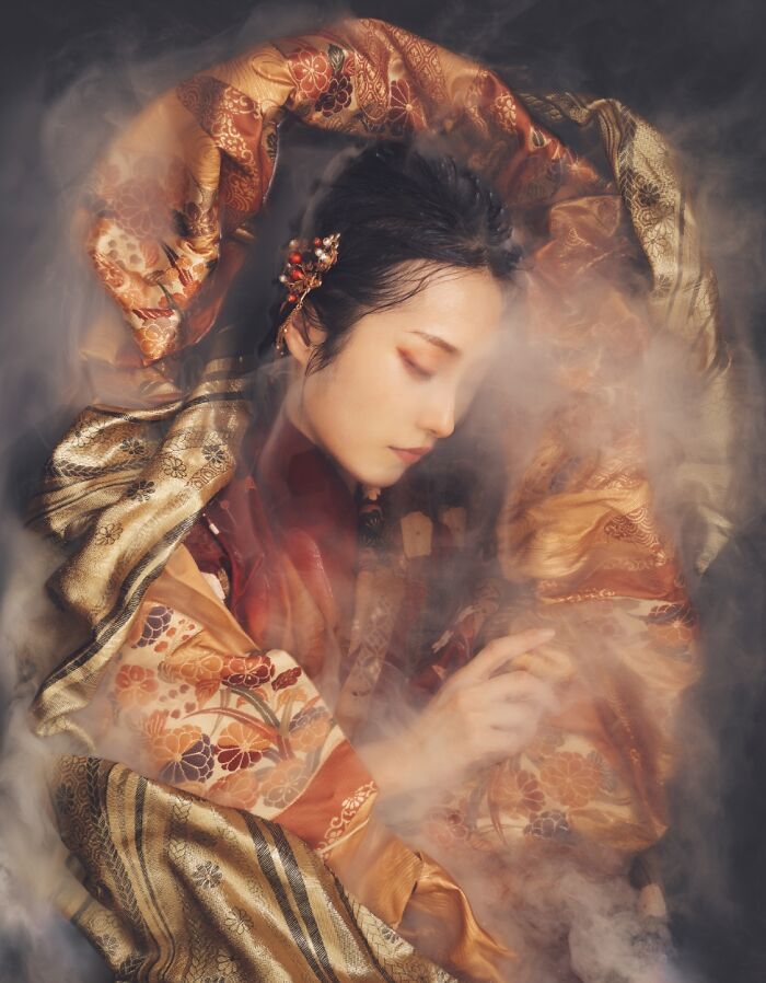 A woman wrapped in ornate fabric with mist, showcasing artistic style from the 2023 Budapest International Foto Awards.