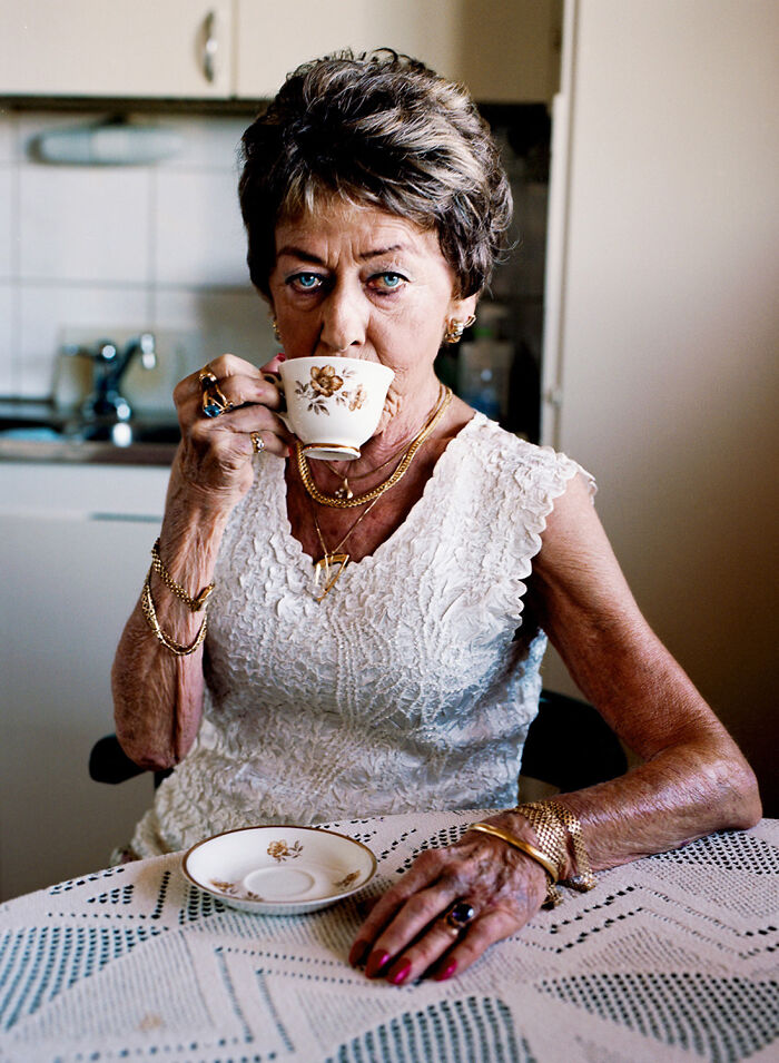 Elderly woman in a lace dress, adorned with gold jewelry, drinking tea, representing 2024 IPA photography winners.