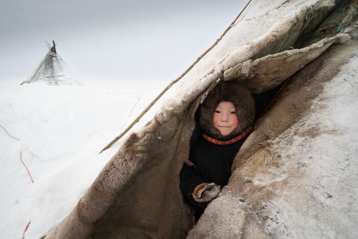 Child in fur coat peeking from a snow-covered tent in an award-winning advertising photo from 2023 Budapest Foto Awards.