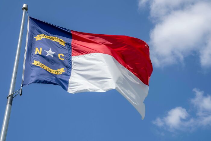 North Carolina flag waving against a blue sky, relating to hilariously inaccurate fact someone told.