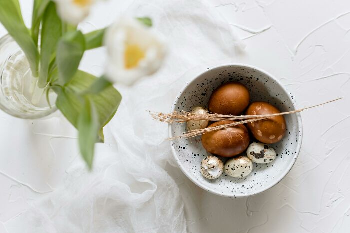 Bowl of brown and speckled eggs on a white table, with a tulip.