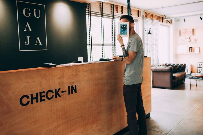 Man holding a book over his face at a check-in desk.