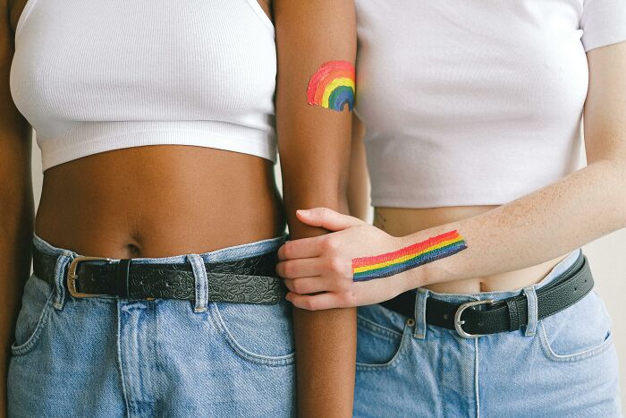 Two people wearing white tops and denim jeans, with rainbow paint on their arms.