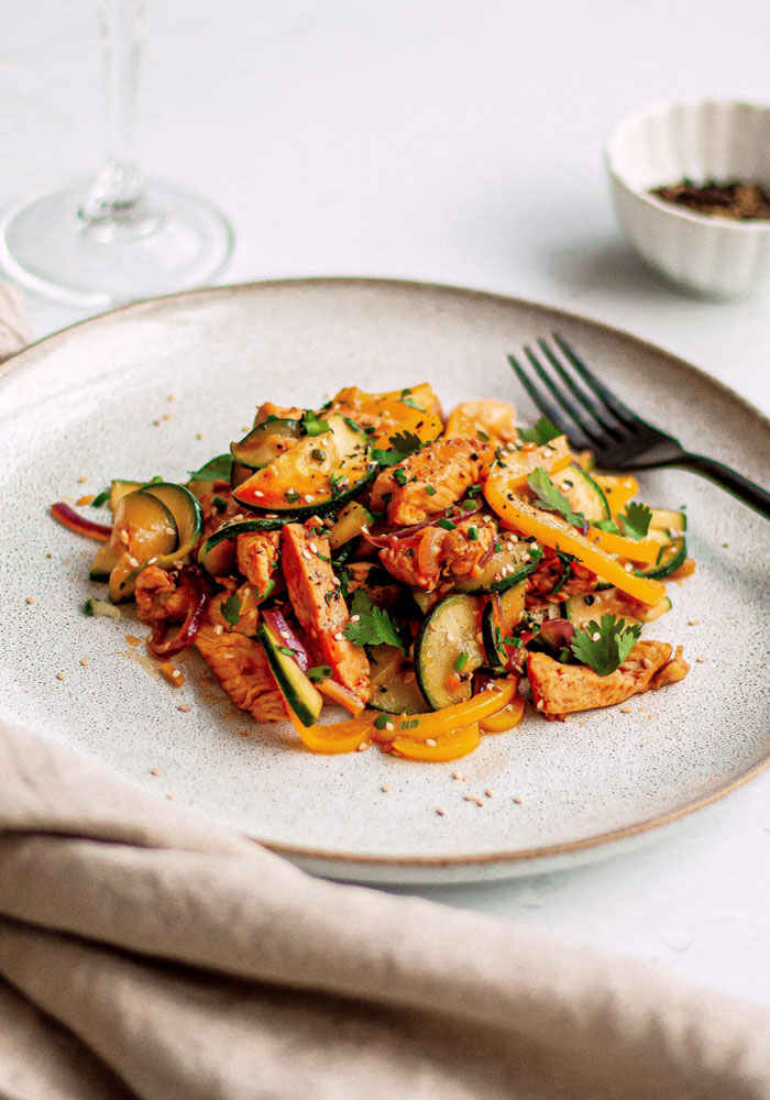 A vibrant lunch idea featuring stir-fried chicken with bell peppers, zucchini, red onions, and fresh herbs, served on a beige plate with a fork.