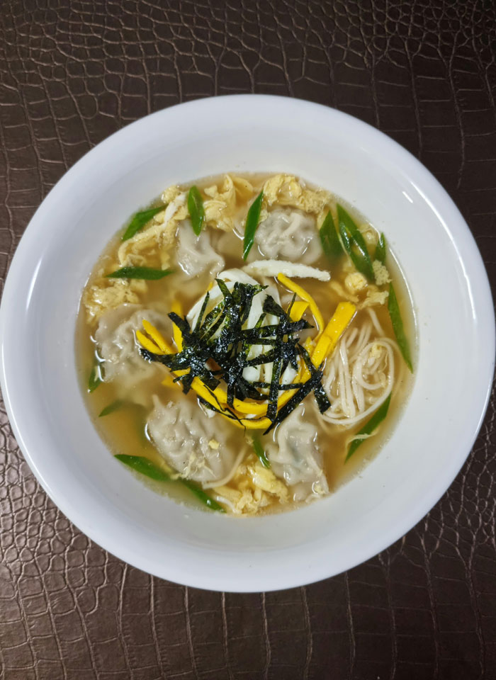 A warm lunch idea featuring a bowl of dumpling soup with noodles, garnished with strips of seaweed, sliced egg, green onions, and enoki mushrooms, served in a light broth.