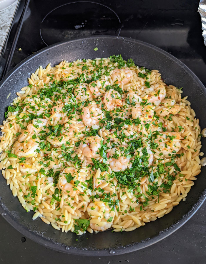 A delicious lunch idea featuring a pan of orzo pasta mixed with shrimp, garnished generously with fresh parsley and a light sauce.