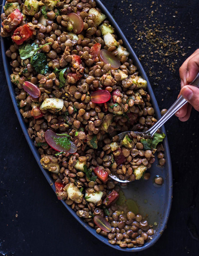 A lunch idea featuring a vibrant lentil salad with grapes, diced veggies, and herbs on an oval plate, ready to be served with a spoon.