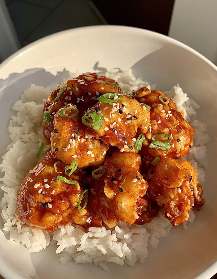 A lunch idea featuring crispy fried cauliflower tossed in a spicy sauce, served on a bed of white rice, topped with sesame seeds and green onions.