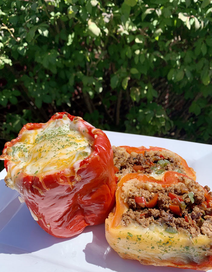 A delicious lunch idea featuring stuffed bell peppers filled with ground beef, vegetables, and melted cheese, served on a white plate with a background of greenery.