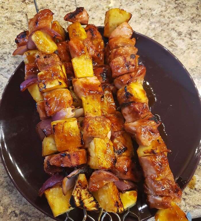 A savory lunch idea featuring grilled skewers of marinated meat, pineapple, and red onions, served on a dark plate with a caramelized glaze.