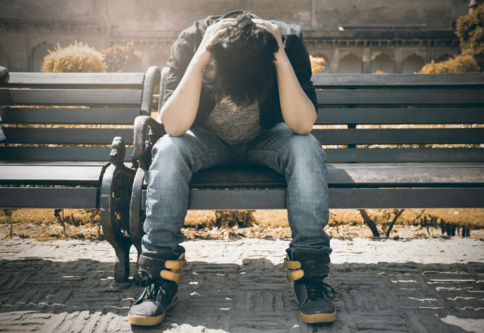 A single dad sitting on a bench, head in hands, reflecting on past college life and hope.