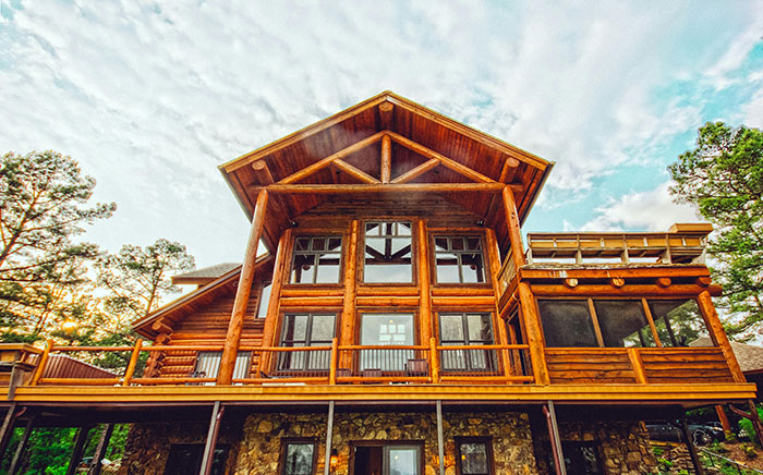 Log cabin with large windows surrounded by trees, under a cloudy sky, representing family dynamics and choice.