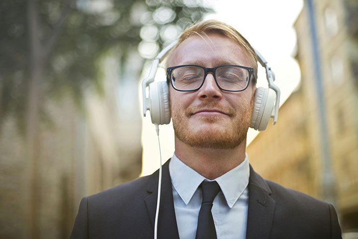 Man in a suit with headphones, enjoying music outdoors with closed eyes.