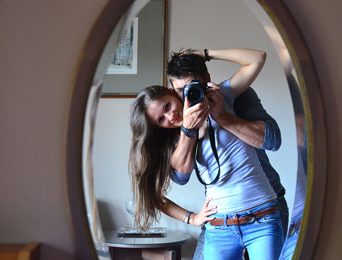 Couple smiling in mirror, woman embraces man with camera.