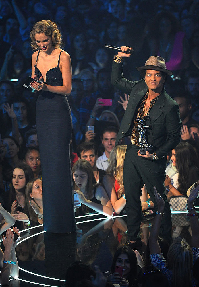 Taylor Swift in a navy dress holding an award, standing beside Bruno Mars, a shorter man in a hat holding a microphone and trophy on stage. How tall is Taylor Swift?