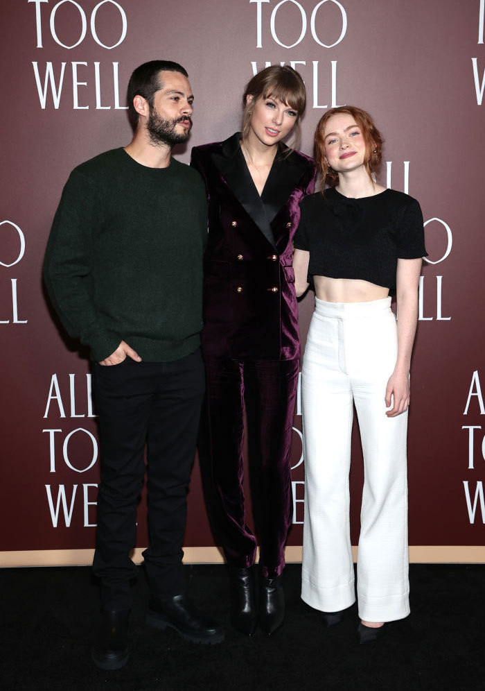 Taylor Swift in a dark velvet suit standing with Dylan O’Brien in a green sweater and Sadie Sink in a black top and white pants. How tall is Taylor Swift?