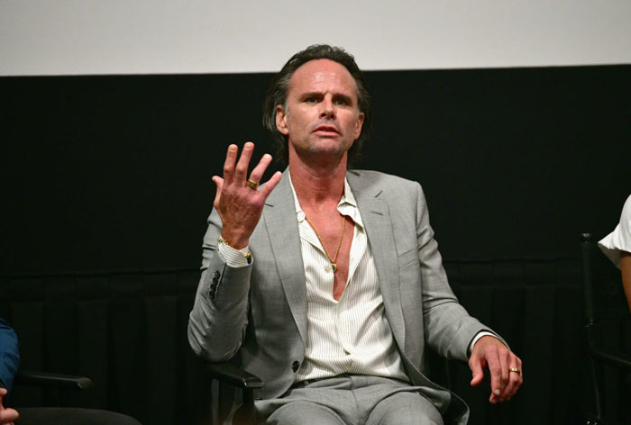  A B list celebrity, Walton Goggins, is speaking passionately while gesturing with his hand during a panel discussion. He is wearing a light gray suit and an open-collared shirt.