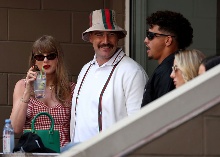 Taylor Swift in a red checkered dress and sunglasses, holding a drink, standing beside Travis Kelce in a white sweater and bucket hat. How tall is Taylor Swift?