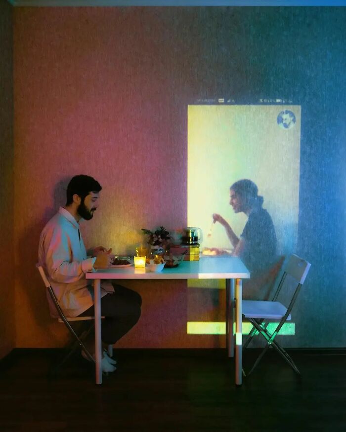 A man dining alone with a projected image of another person on the wall, creating a surrealism effect.