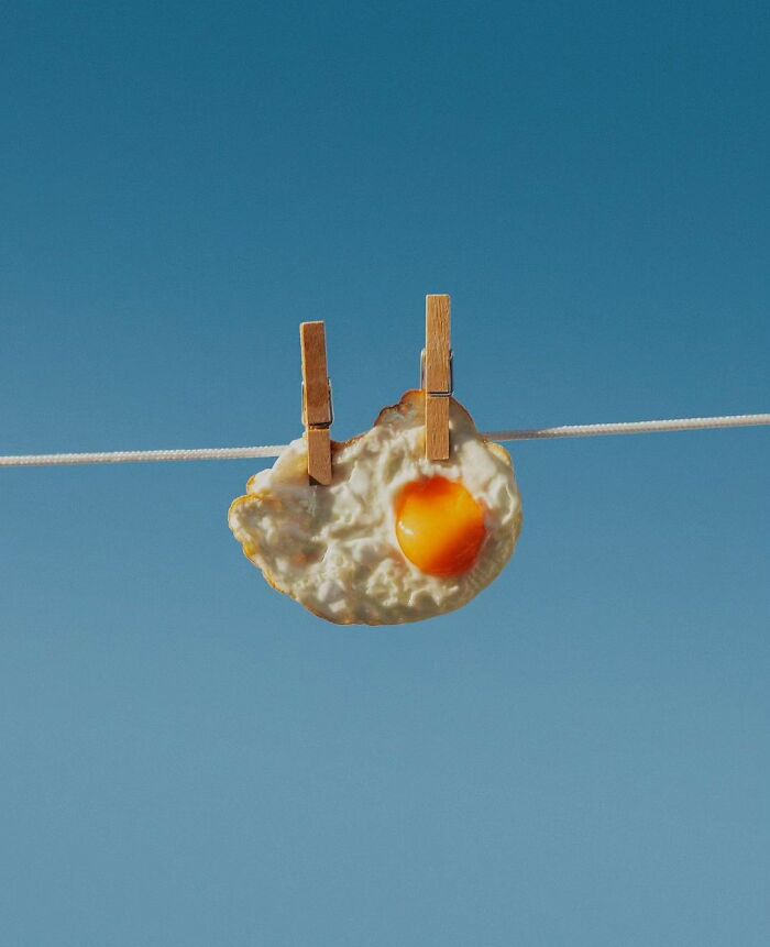 A fried egg attached to a clothesline with clothespins against a clear blue sky, showcasing surrealism.