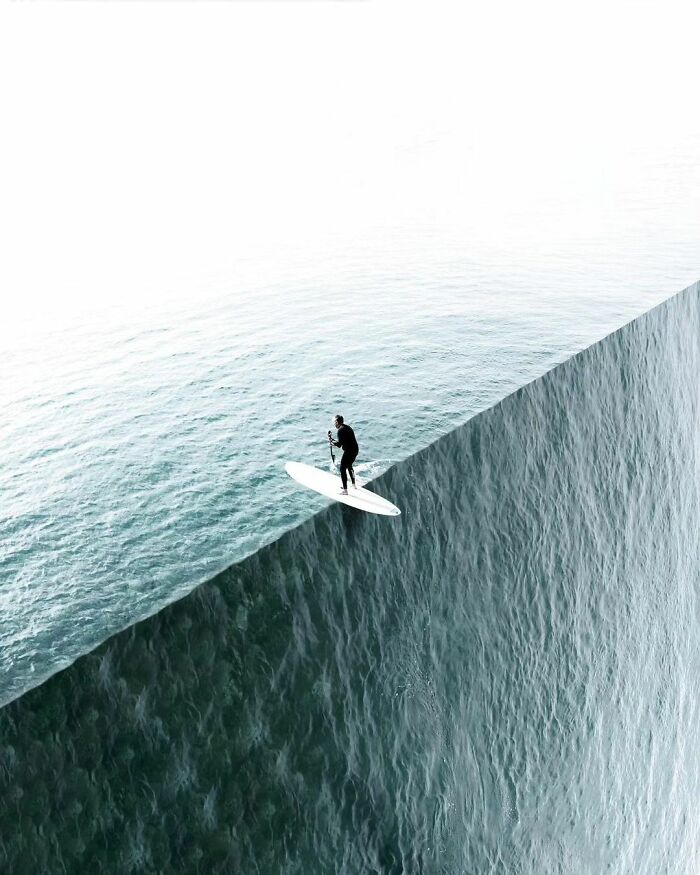 Surrealism image of a person paddleboarding on an ocean edge.