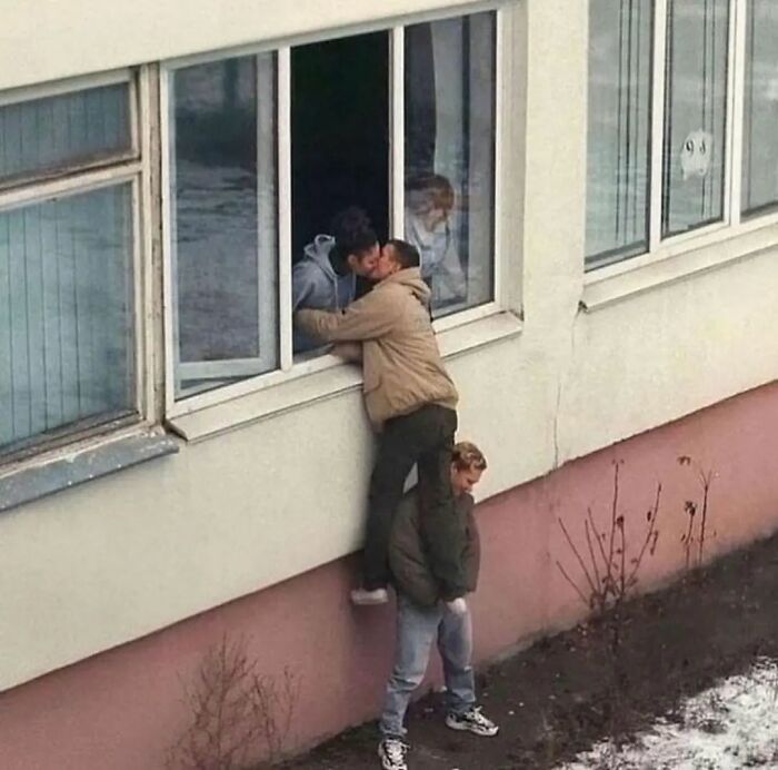 Three people creatively manage a kiss through a window, capturing an adorable and weird moment for Instagram.