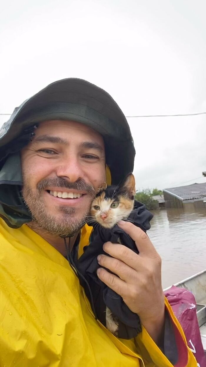 Man in a raincoat smiling, holding a kitten, embodying the hero without a cape spirit amidst floodwaters.