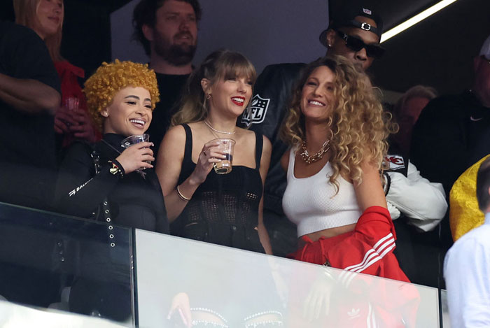 Taylor Swift in a black outfit holding a drink, standing with Ice Spice and Blake Lively at a sporting event. How tall is Taylor Swift?