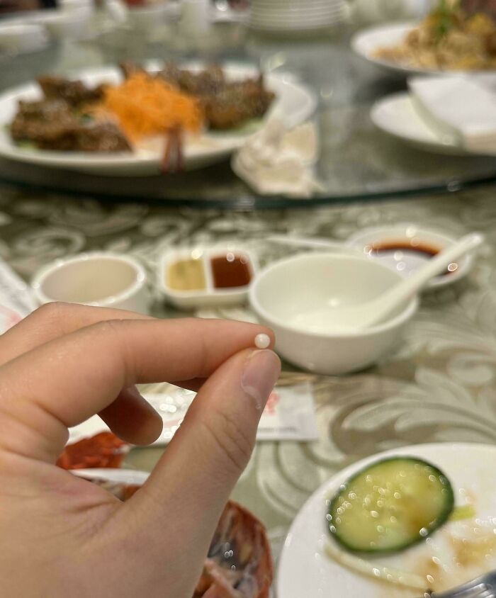 Hand holding a tiny pearl found in food at a restaurant, displaying a mildly interesting discovery.