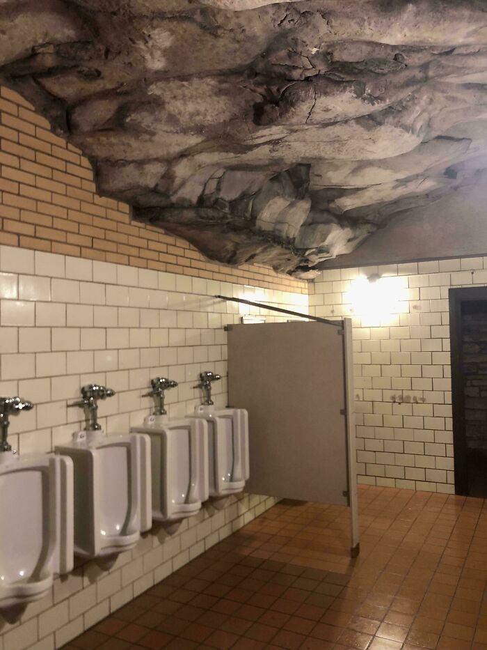 Public bathroom with rocky ceiling, featuring urinals and tiled walls; a mildly interesting architectural choice.