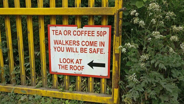 UK humor sign: "Tea or Coffee 50p. Walkers come in, you will be safe. Look at the roof," on a yellow gate.