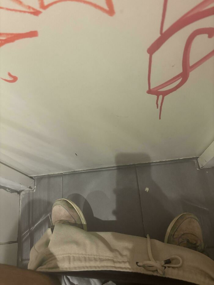 Mildly interesting restroom graffiti above tile floor, sneakers visible in corner.