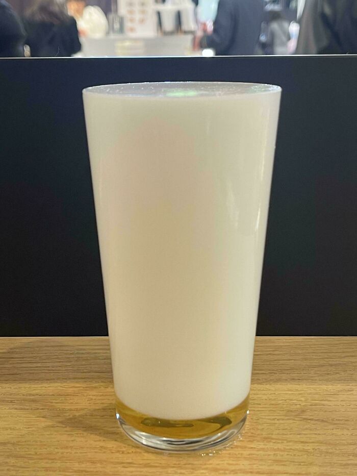 A glass of milk with foam on wood table, capturing a mildly interesting moment.