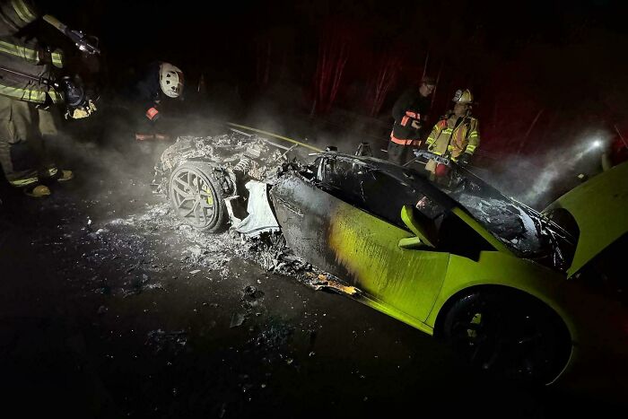 Firefighters assess a burned luxury car after an expensive incident at night.