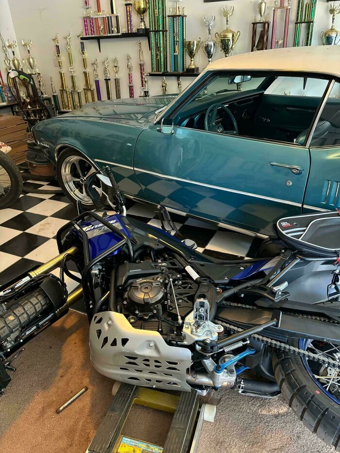 Motorcycle accident in a garage with a vintage car and numerous trophies, suggesting an unfortunate and costly incident.