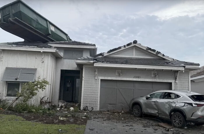 Damaged house with dumpster on roof and a dented car, illustrating unfortunate expensive incidents.