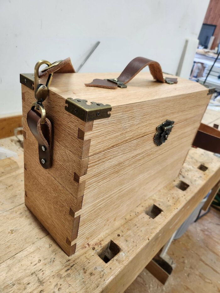 Woodworking project featuring a handcrafted wooden box with leather straps and metal accents on a workbench.