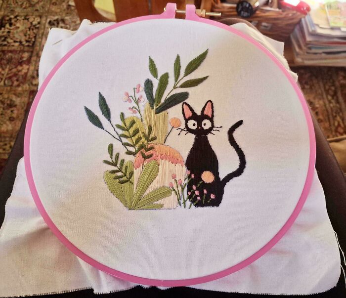 Creative embroidery featuring a black cat and greenery in a pink hoop.