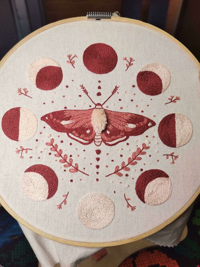 Creative embroidery of a moth with moon phases and floral elements on fabric.