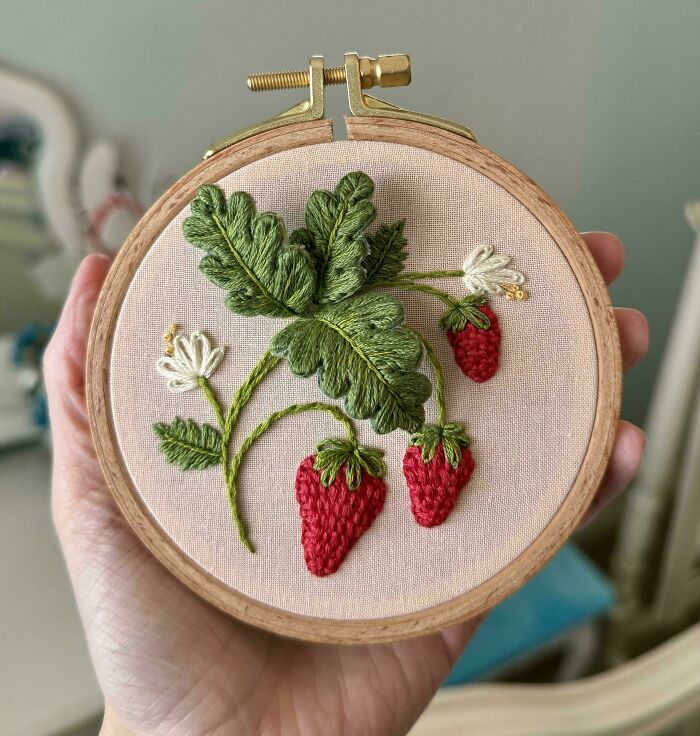 Creative embroidery with strawberries and leaves on a fabric hoop, handcrafted with fine detail.