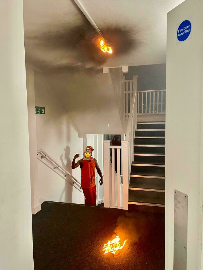 A person in a hallway with small fires burning on floor and ceiling, embodying quirky British humor.