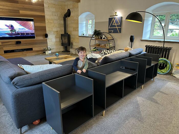 Child playing near a sofa with custom woodworking shelves in a cozy living room.