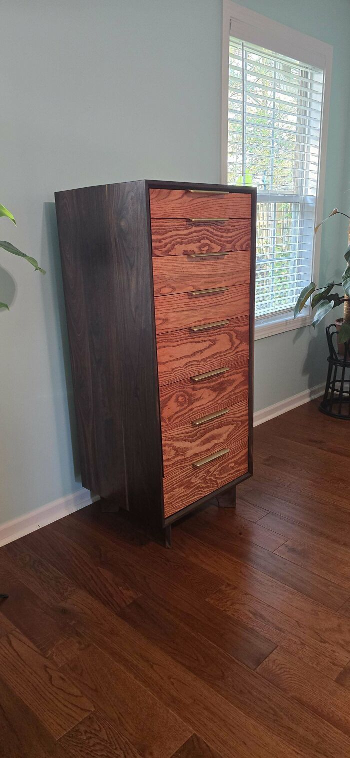 Woodworking project featuring a tall dresser with contrasting wood finishes, in a room with wooden floors and a large window.