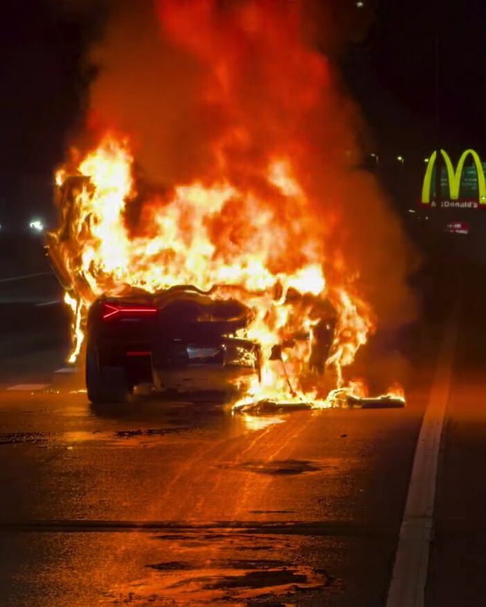 A car engulfed in flames on a road at night, near a McDonald's sign, illustrating an expensive unfortunate incident.