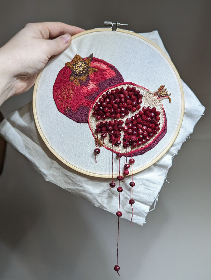 Creative embroidery of a pomegranate in a hoop, showcasing detailed beadwork and vibrant colors.