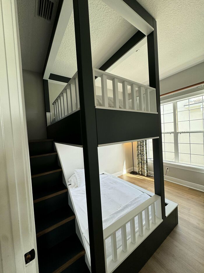 Two-level black and white wooden bunk bed with stair access, showcasing impressive woodworking design.