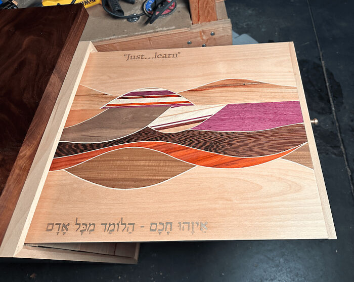 Woodworking project featuring colorful wood inlays and the engraved phrase "just...learn" in a workshop setting.