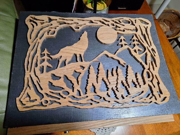 Intricate woodworking project featuring a wolf howling at the moon, surrounded by trees and mountains.